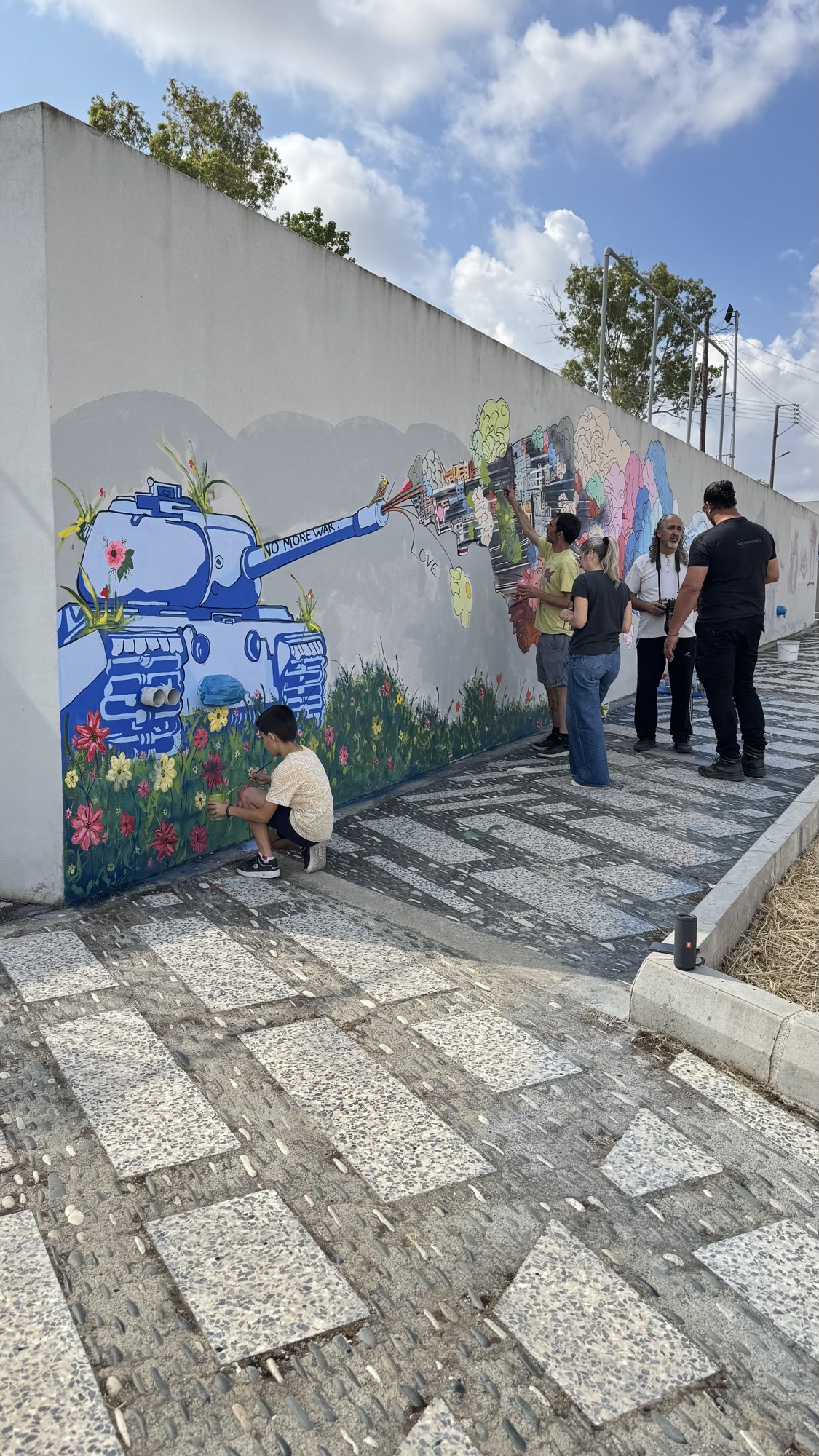 The mural wall with the tank, as people gather to paint